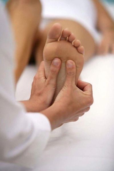 Hands massaging a foot on a white surface; reflexology treatment.
