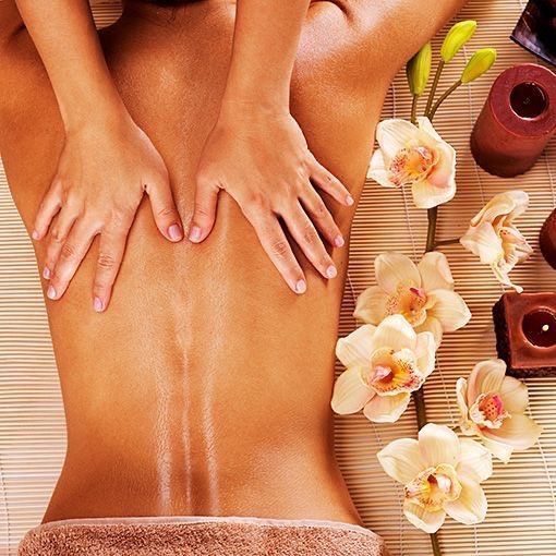 Hands giving a back massage on a person's back, spa setting with flowers and candles.