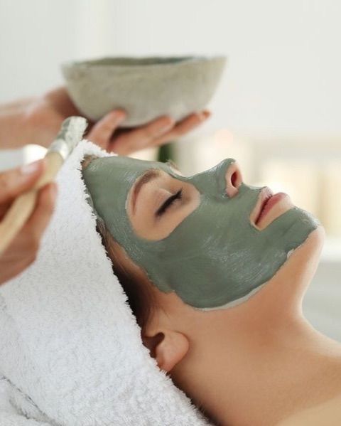 Woman with eyes closed, receiving a facial mask application in a spa setting.