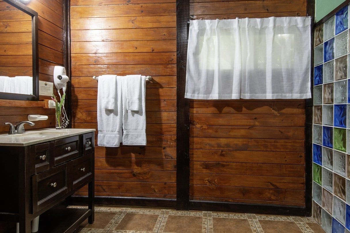 Bathroom with wood-paneled walls, white towels, a dark vanity, and a shower with colorful tiles.