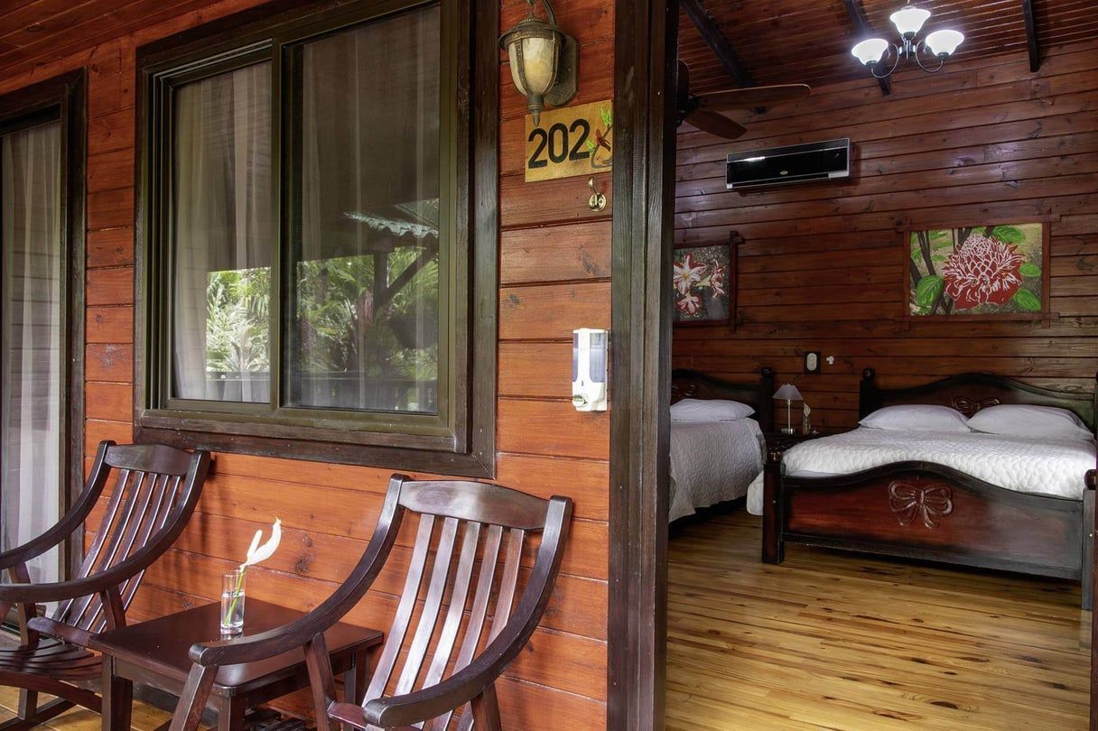 Wooden cabin entrance with chairs and a view of two beds inside.