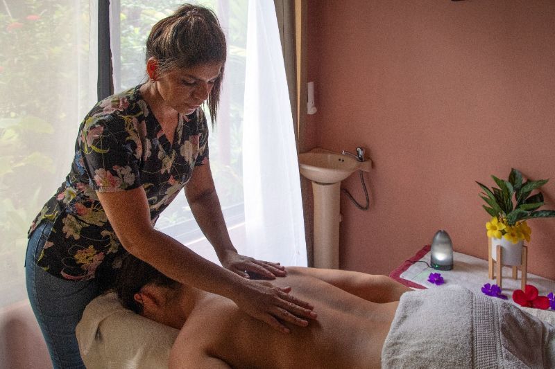 Woman giving a back massage in a spa. She is wearing a floral top and jeans.