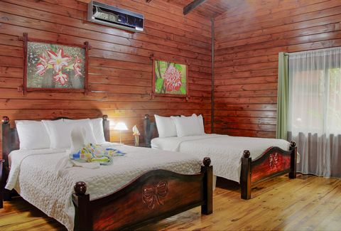 Bedroom with two beds, wooden walls, floral artwork, and a window with sheer curtains.