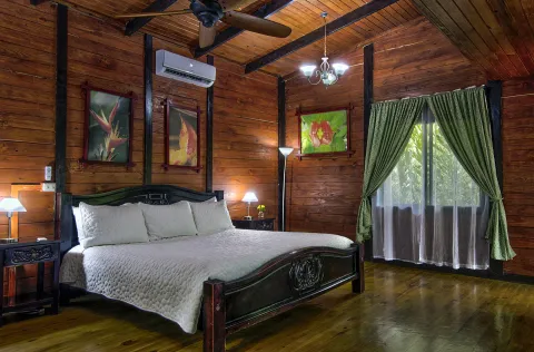 Wooden bedroom with large bed, art, green curtains, and a ceiling fan.