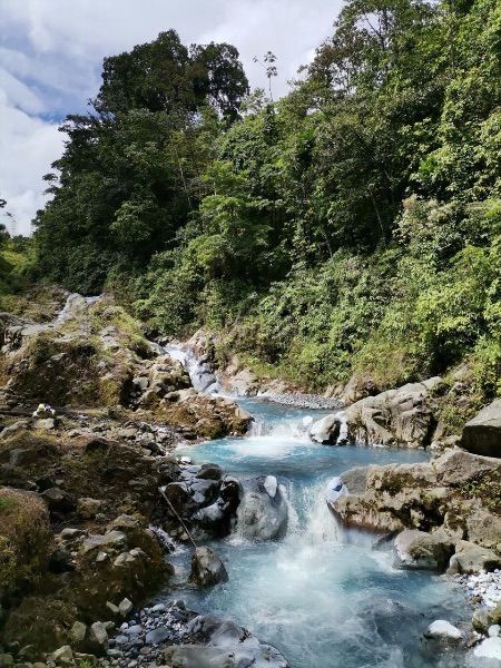 Blue river flowing through rocky terrain, surrounded by lush green foliage.