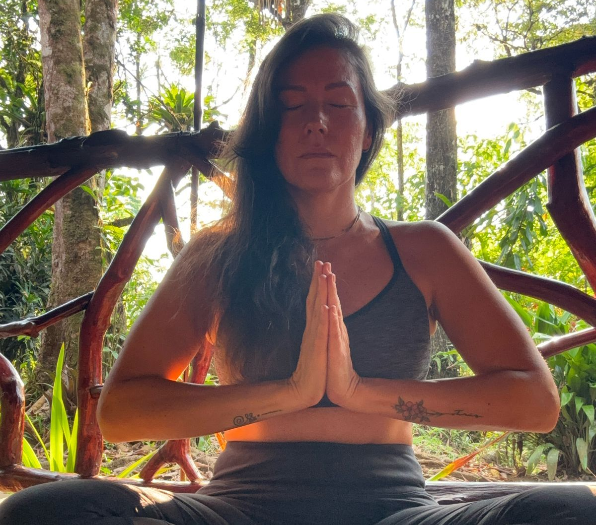 Man in yoga pose on mat, arms raised, outdoor wooden setting.