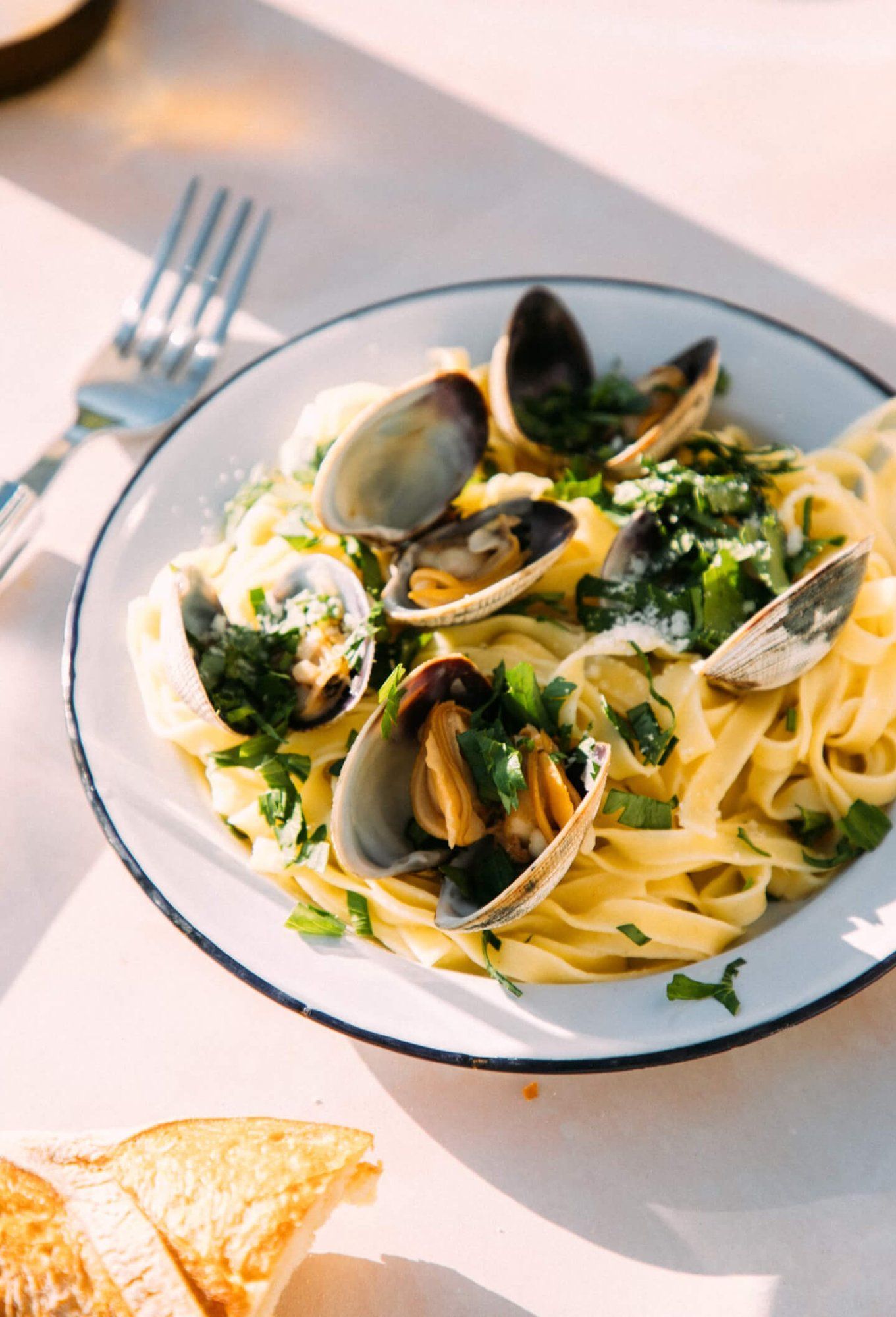 Pasta with clams, garnished with herbs, on a white plate with a blue rim.