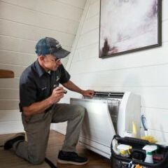 A man is kneeling on the floor working on an air conditioner.