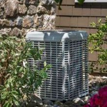 An air conditioner is sitting in front of a stone wall.