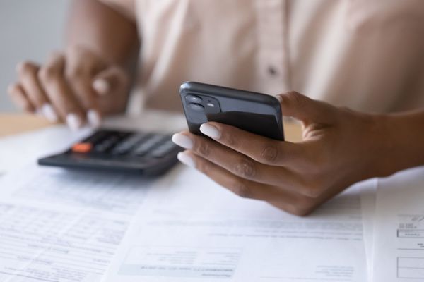 Hands using a smartphone beside a calculator and paperwork on a desk