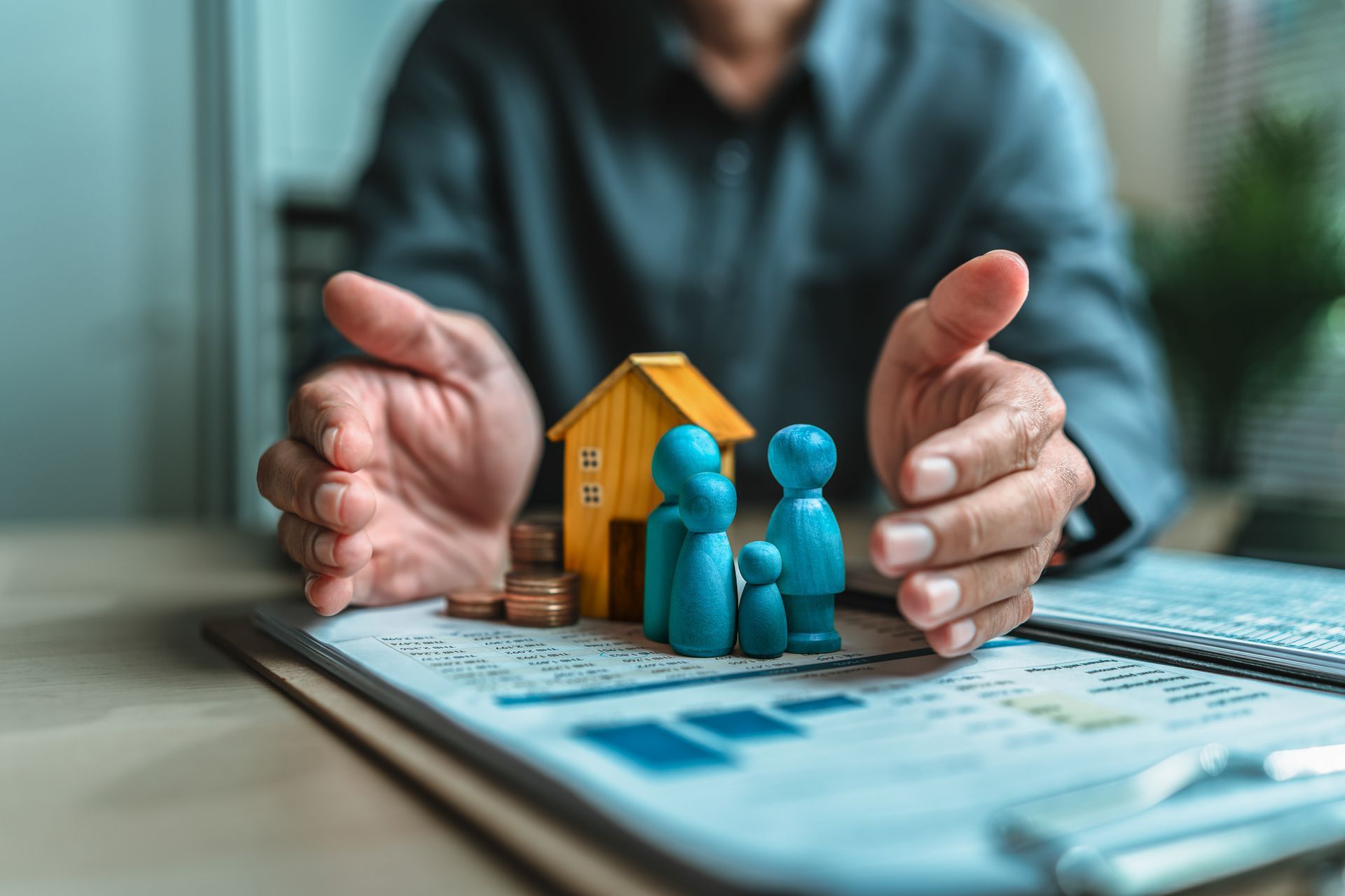 Hands framing small house and figures on documents, suggesting real estate planning or investment