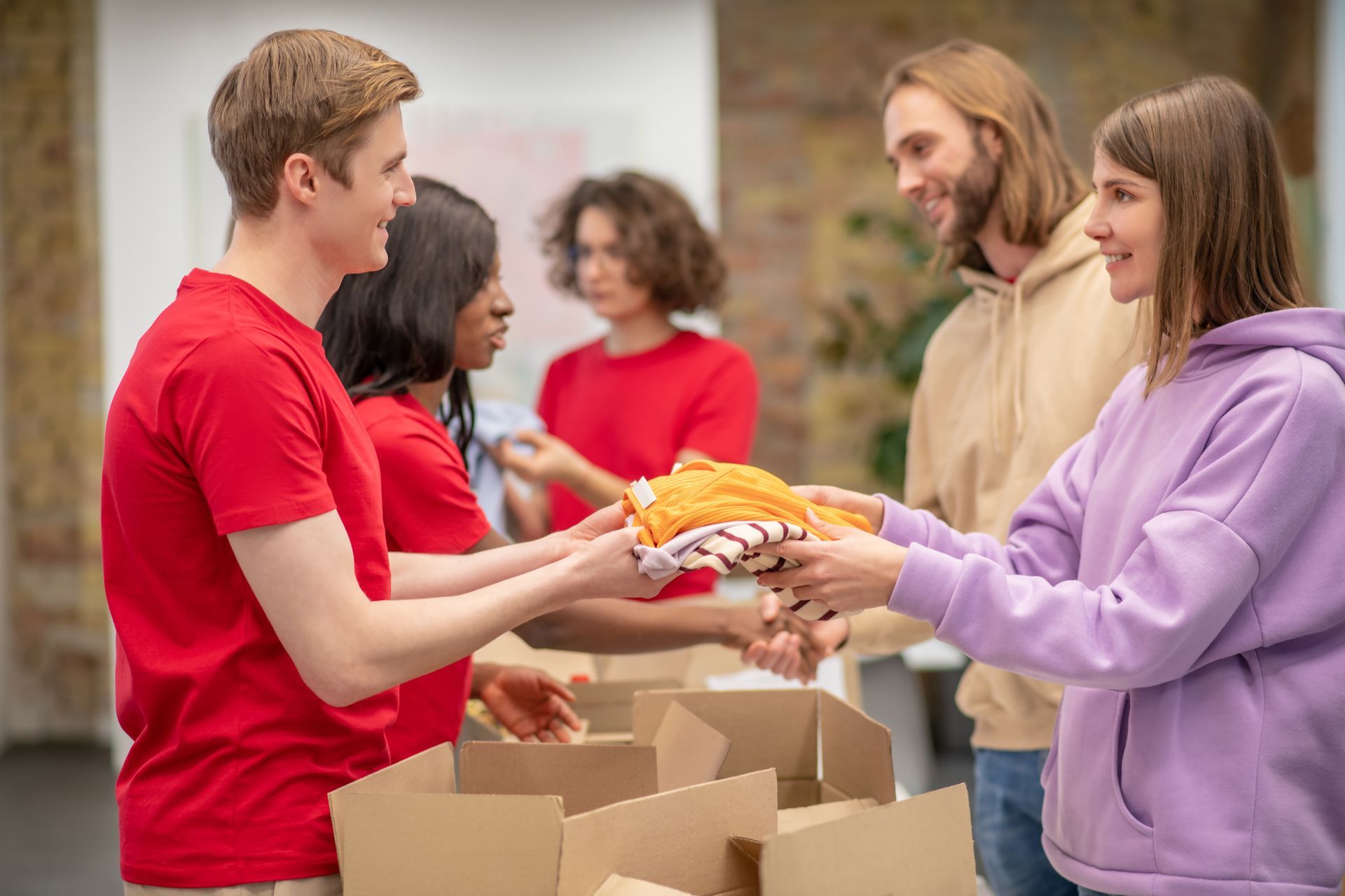 Volunteers in red shirts sorting clothes into boxes, giving to a woman in purple.