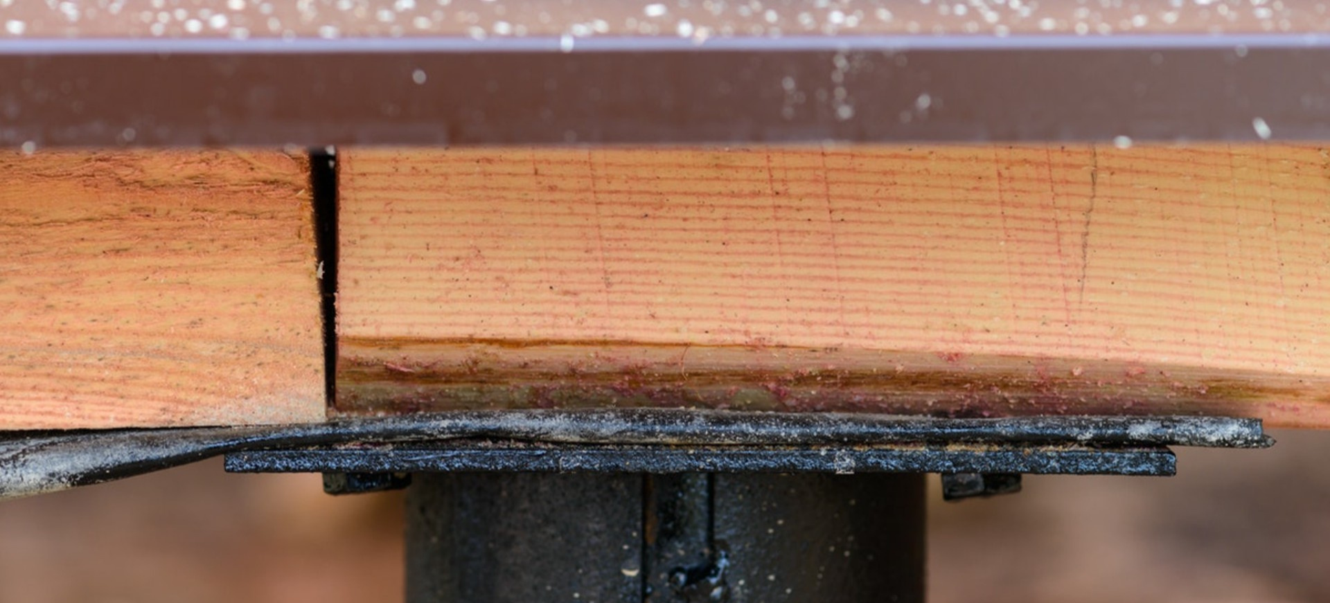 Close-up of a wooden joint with a black metal bracket and fastener underneath.
