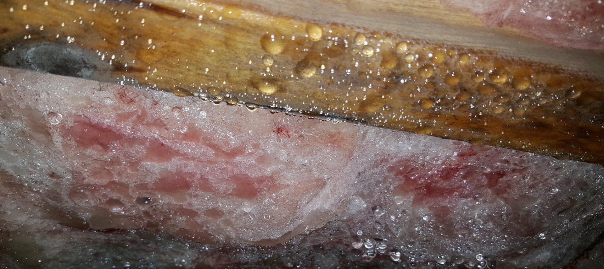 Close-up of a rusty metal surface with pinkish-red corrosion and frost or snow along the bottom edge
