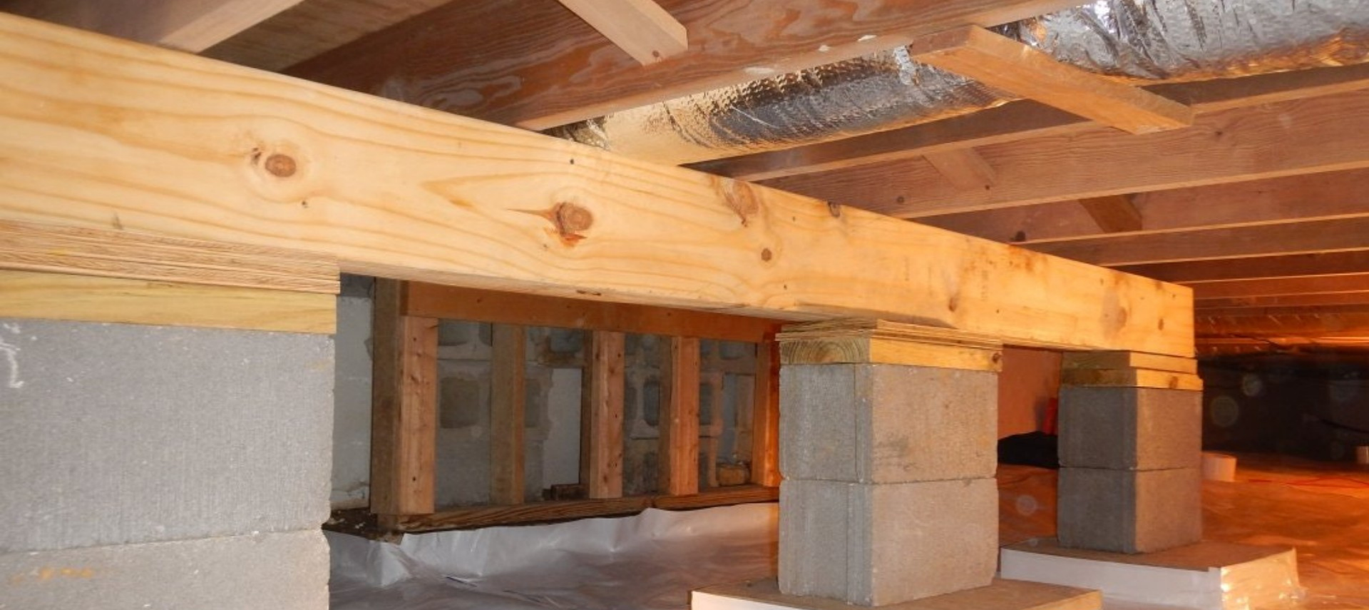 Wooden beam and concrete supports under a house in an unfinished crawl space