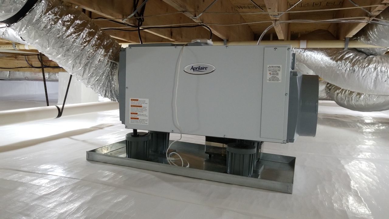Large HVAC unit in an attic, mounted on a metal platform with ductwork overhead.