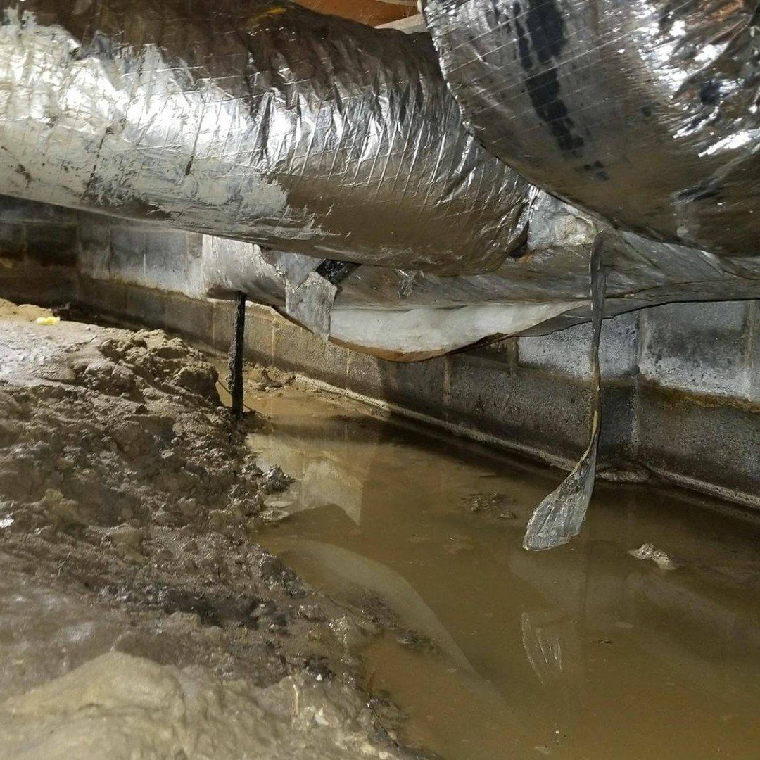 Flooded crawl space with standing muddy water, exposed ducts, and damaged insulation under a house