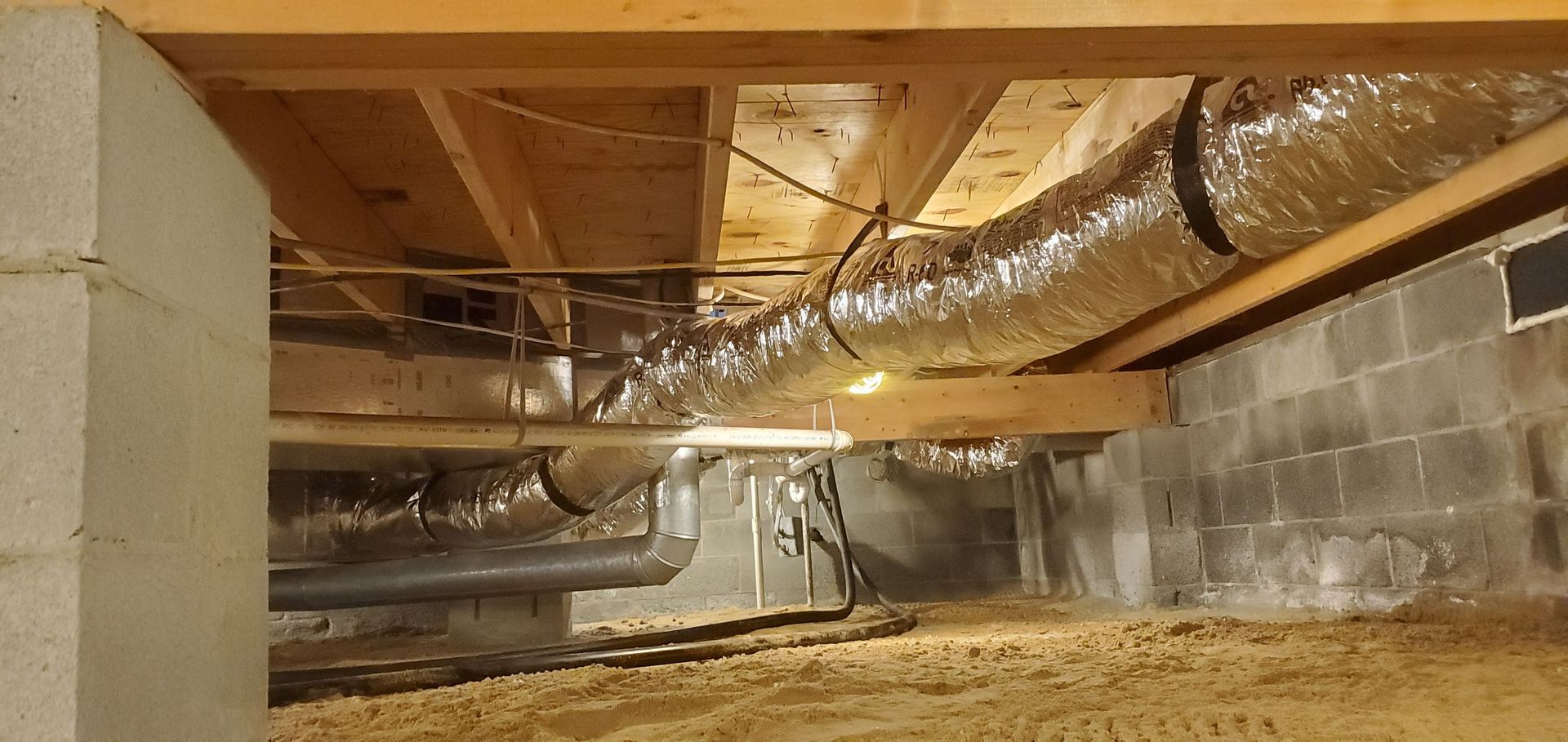 Crawlspace with exposed wooden beams, cinder block wall, and insulated HVAC ducting overhead.