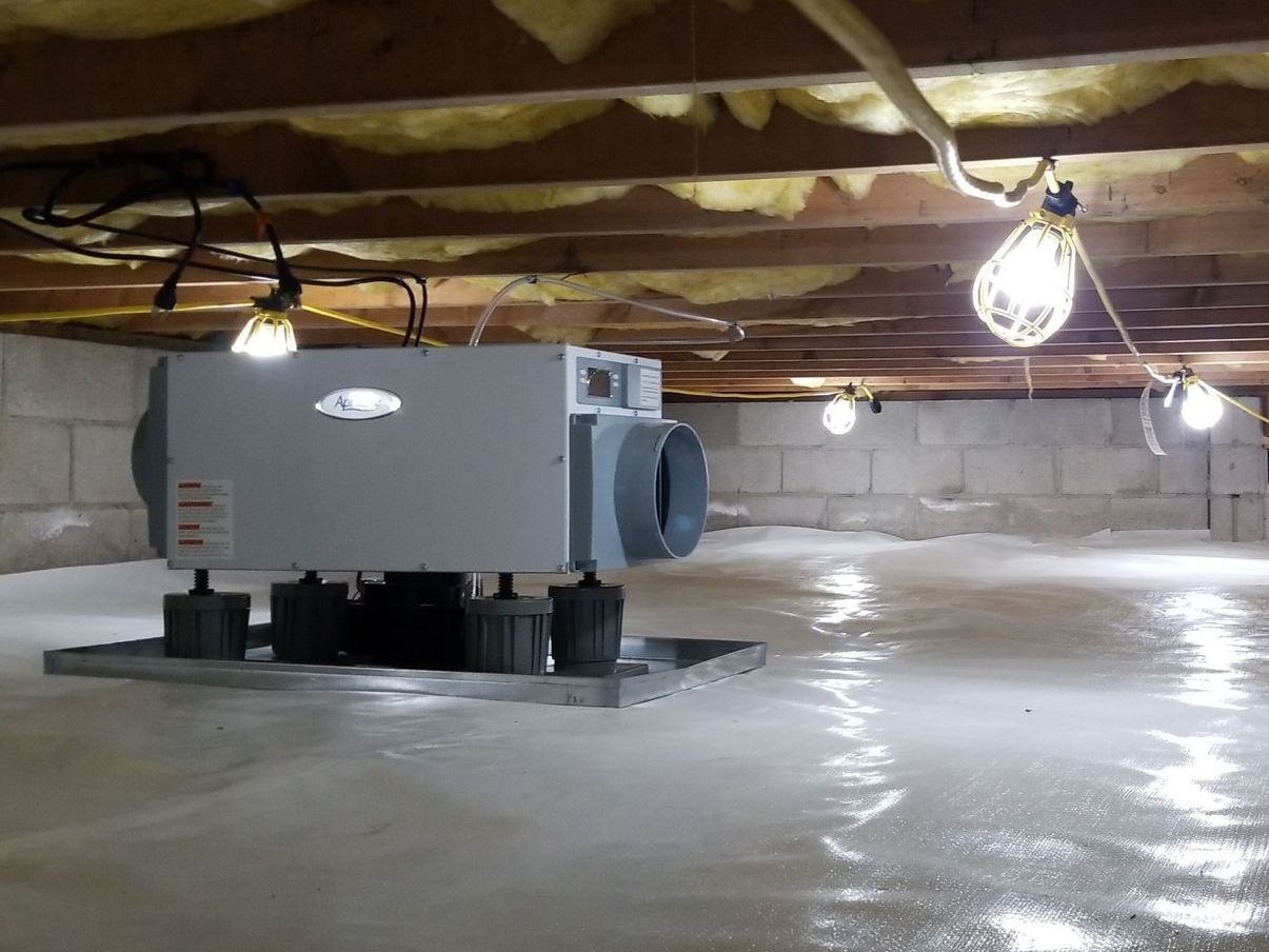 Rectangular HVAC unit in a crawlspace under exposed wooden beams and hanging light bulbs.
