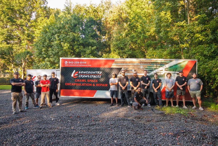 Group of people posing outdoors in front of a red event banner and trees on gravel.