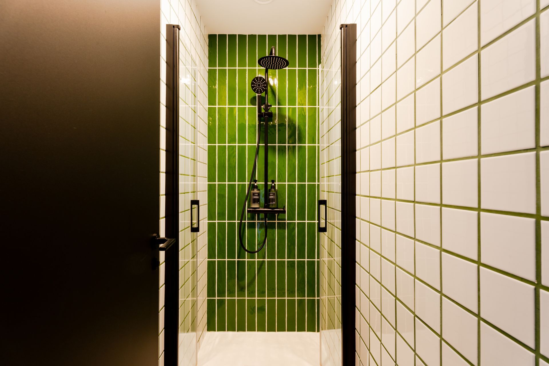A bathroom with green tiles and a black shower head.