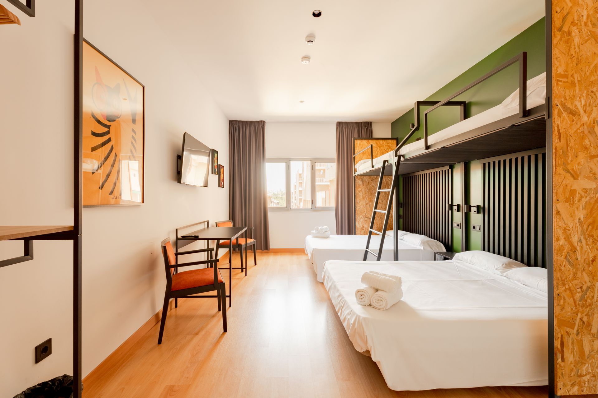 A hotel room with bunk beds , a desk and chairs.
