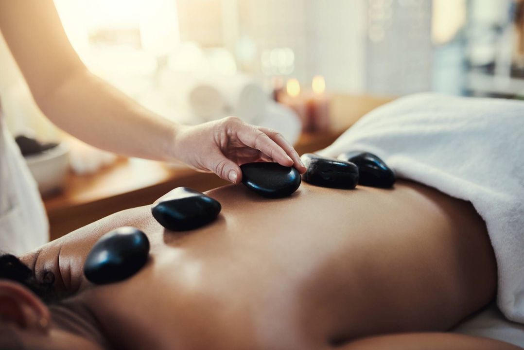Hot stone massage with black stones placed on a person’s bare back by a therapist