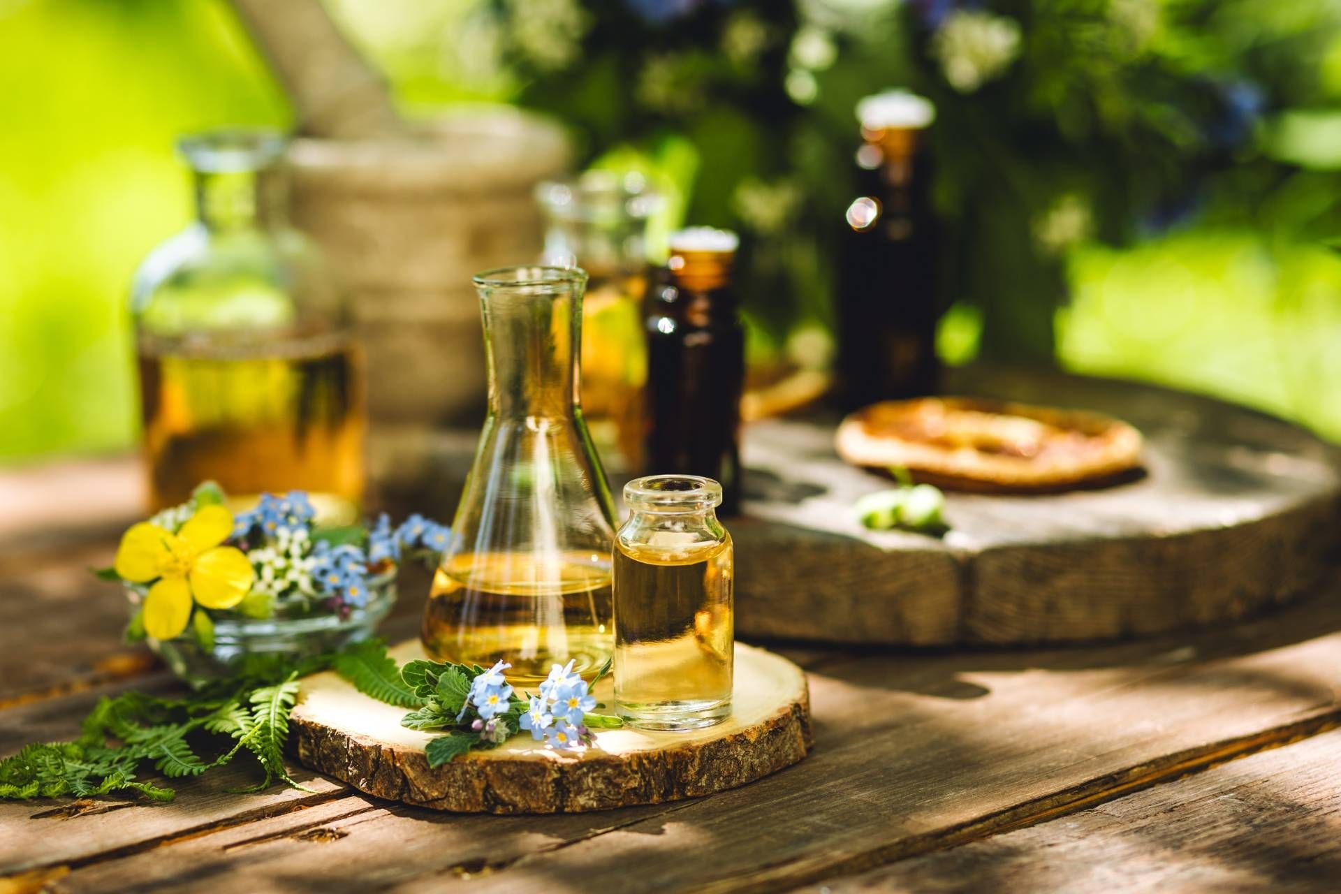 Rustic outdoor table with bottles, glasses, flowers, and a wooden tray in sunlight