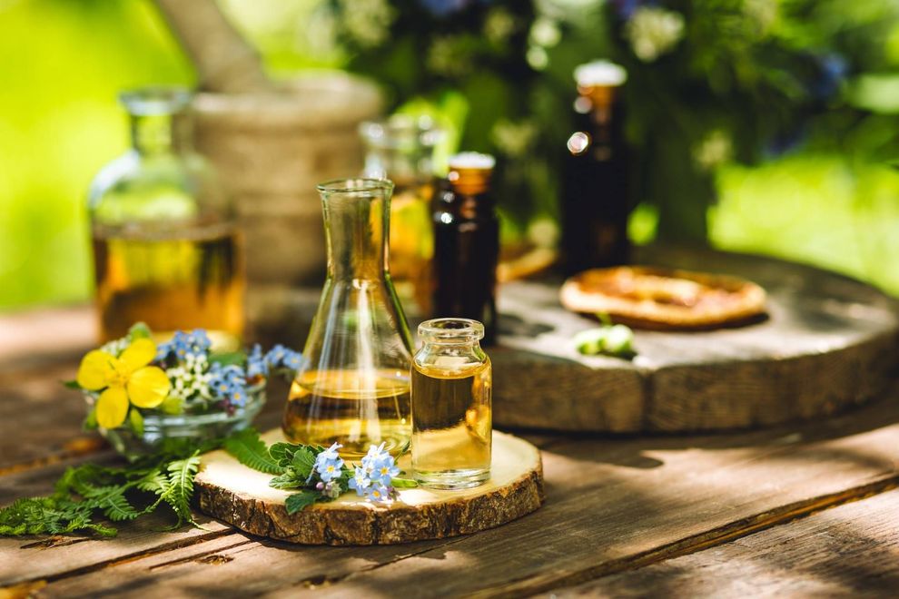 Rustic outdoor table with bottles, glasses, flowers, and a wooden tray in sunlight