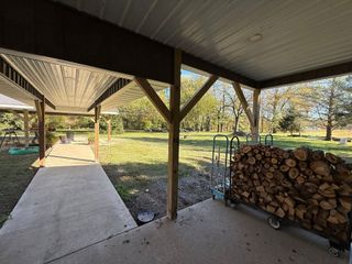 A concrete patio under a covered porch roof with a large rack of stacked firewood beside wooden support beams.