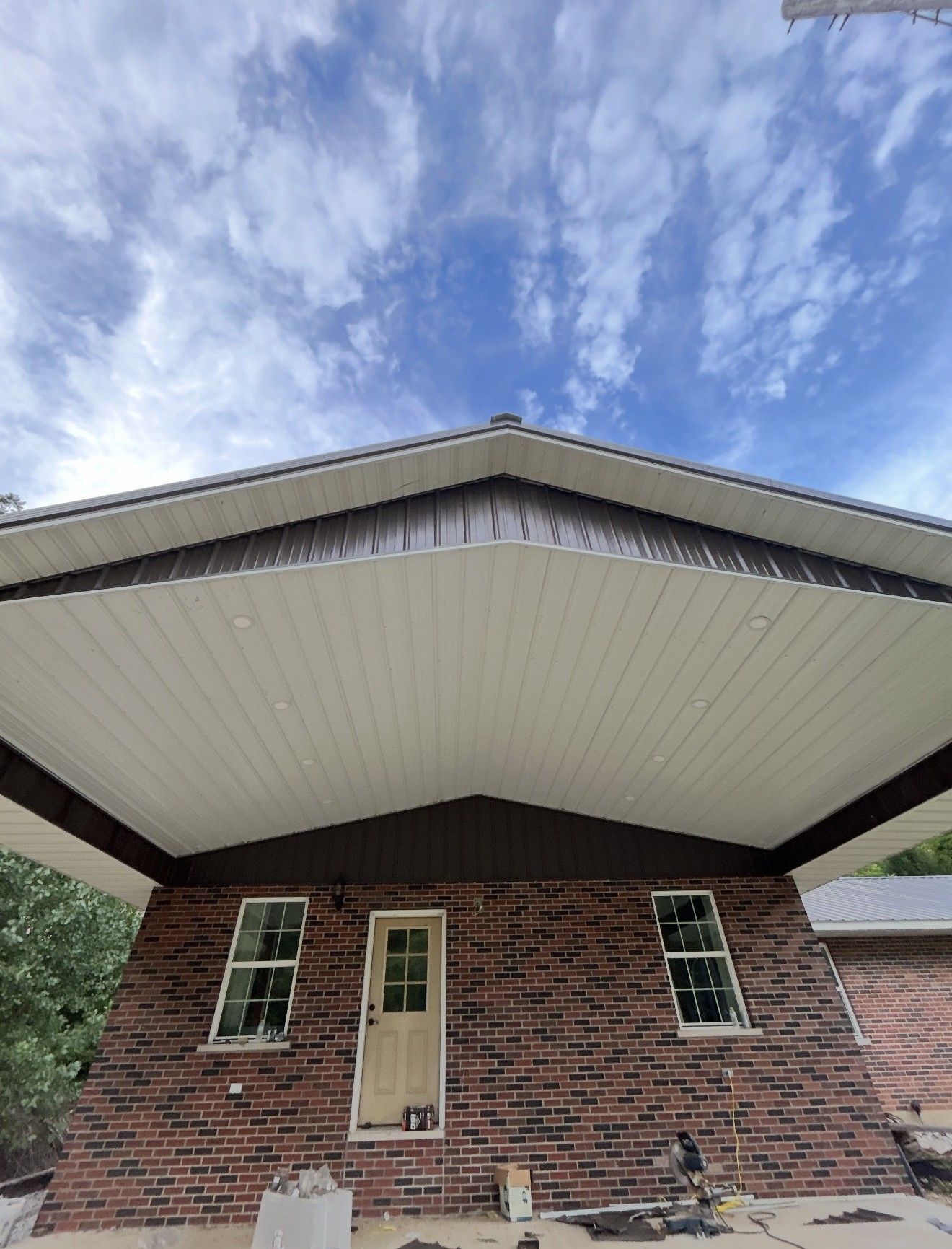 Low-angle view of a red brick house exterior with a prominent gabled roof overhang and white soffit ceiling.