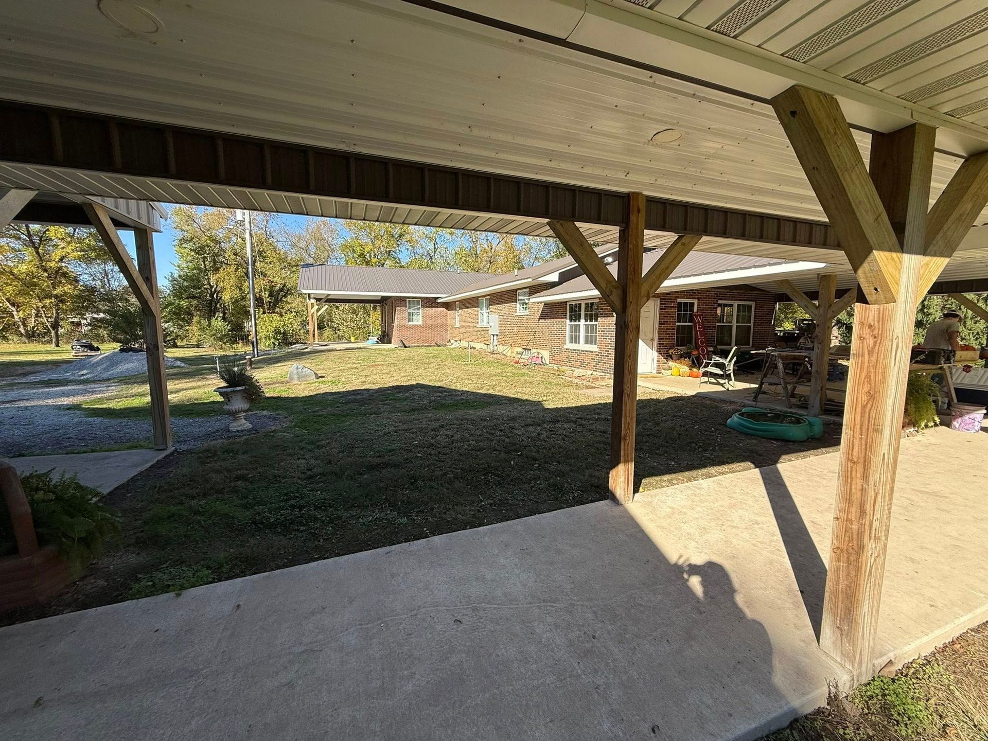 A covered porch looking out toward a one-story residential home and lawn on a sunny day.