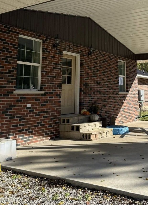 A red brick house exterior featuring a beige door with concrete block steps on a patio under a brown roof overhang.