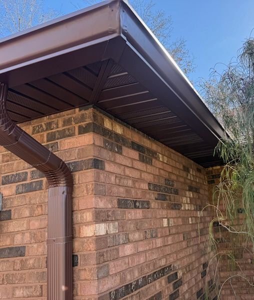 A brown metal gutter and soffit system installed on the corner of a brick residential building exterior.