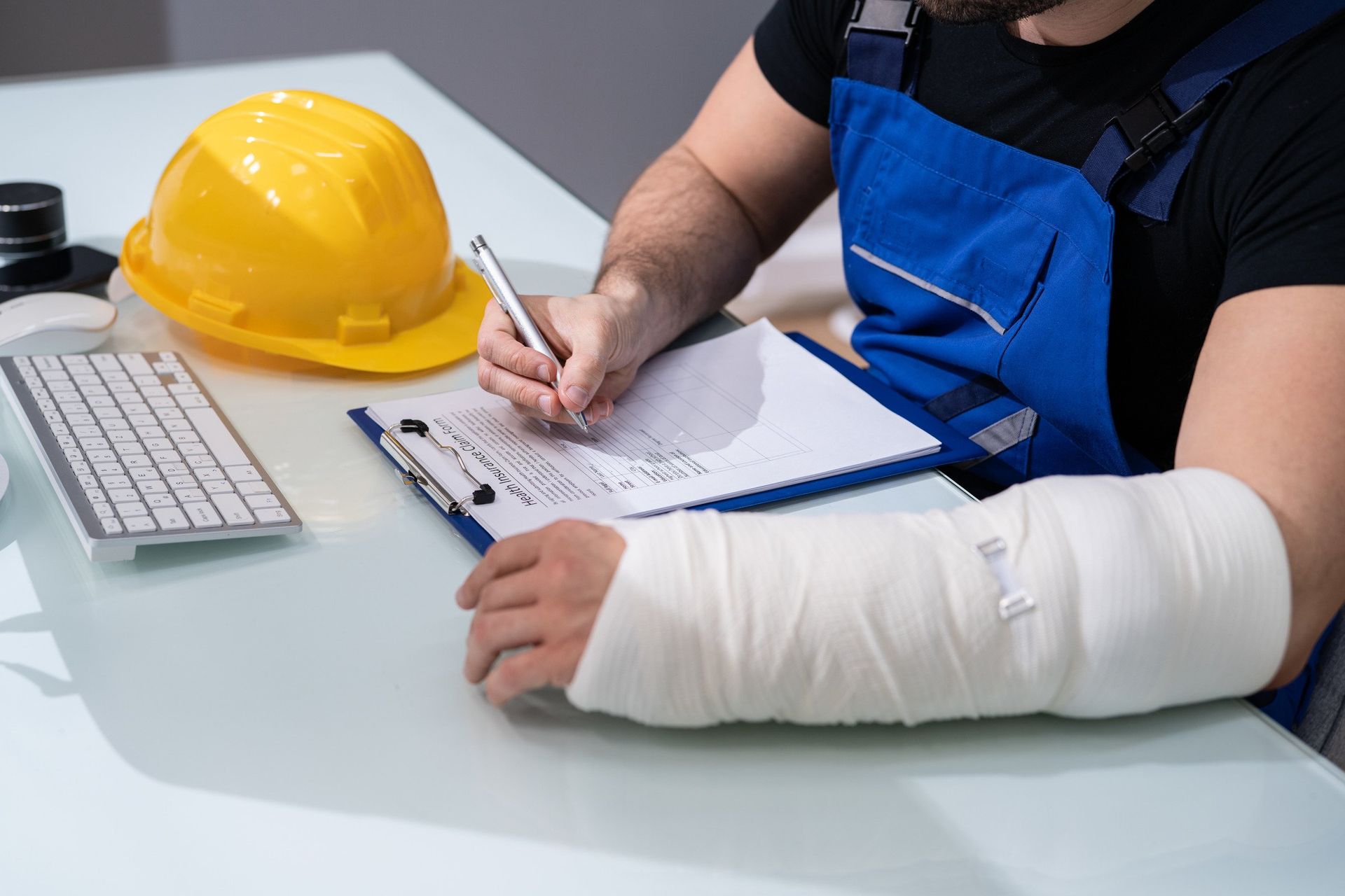 A man with a cast on his arm is sitting at a desk writing on a clipboard.