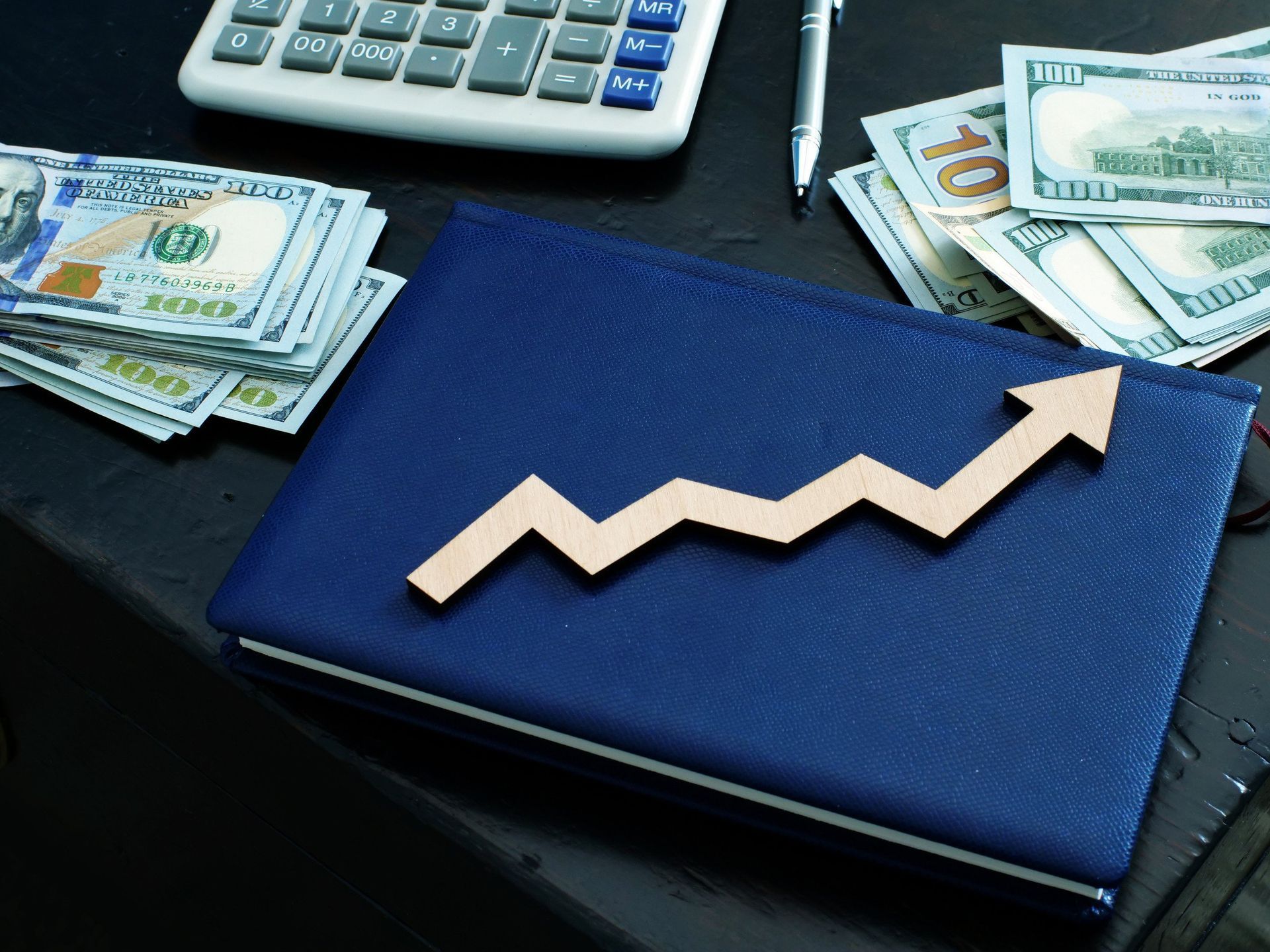 A blue book with an arrow pointing up next to a pile of money and a calculator