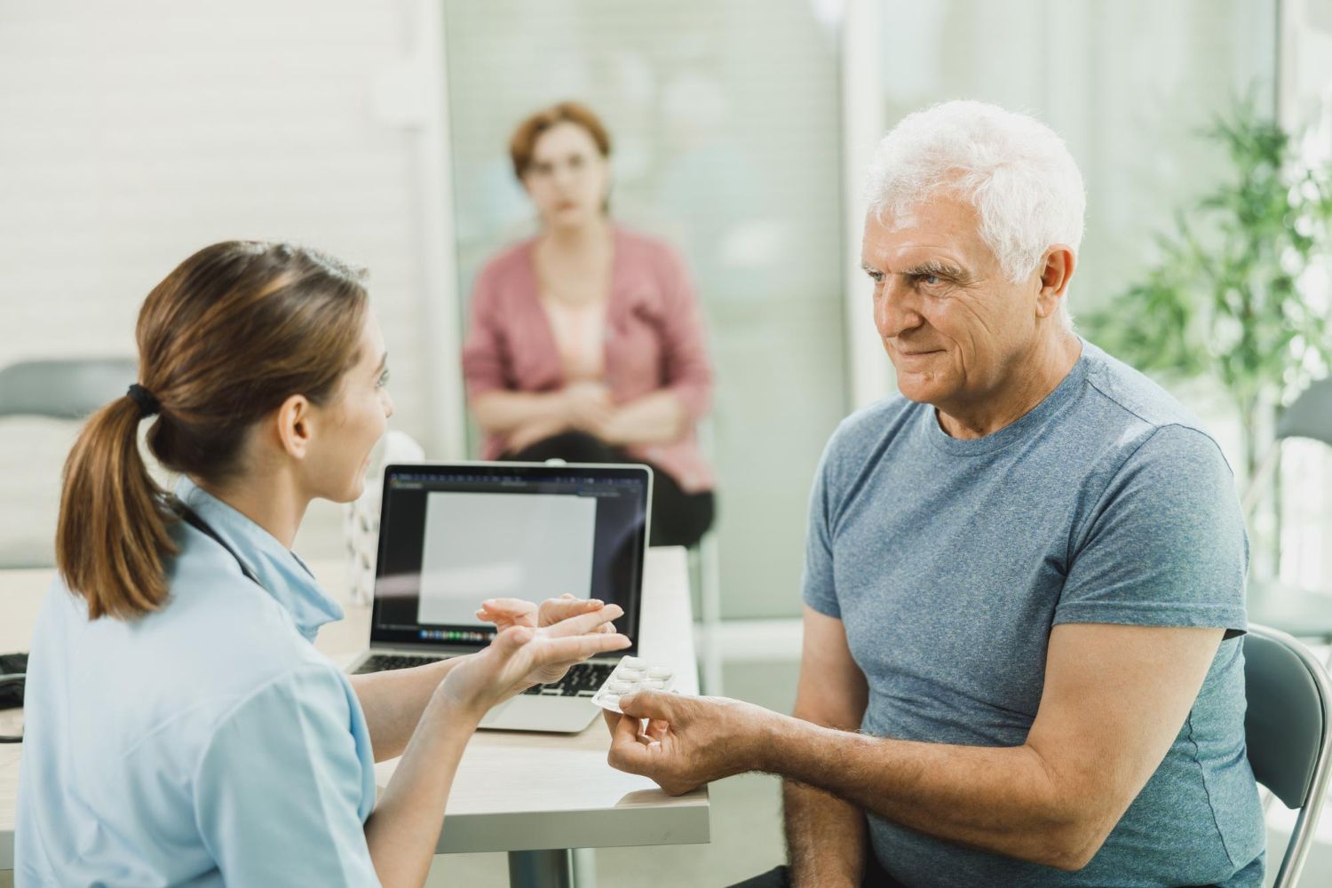 Doctor showing pills to a patient in an office, a person observing.