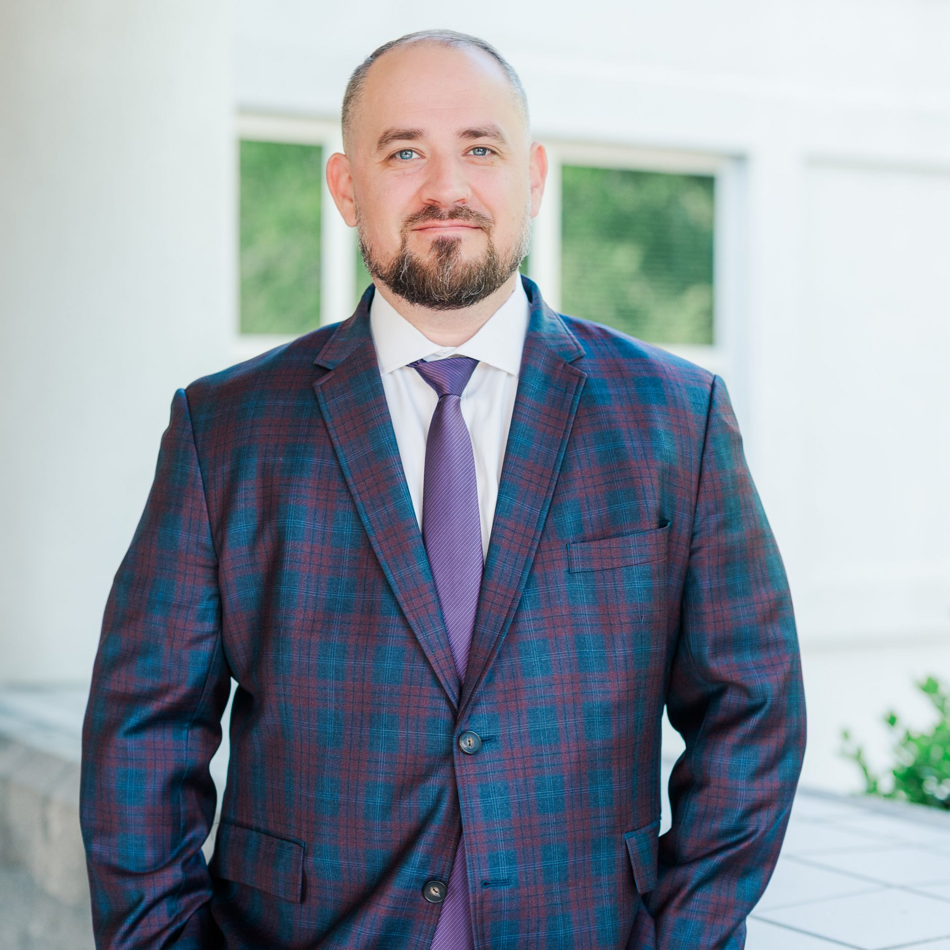 Man with brown hair and beard, wearing a patterned bow tie and blue suit, smiles.
