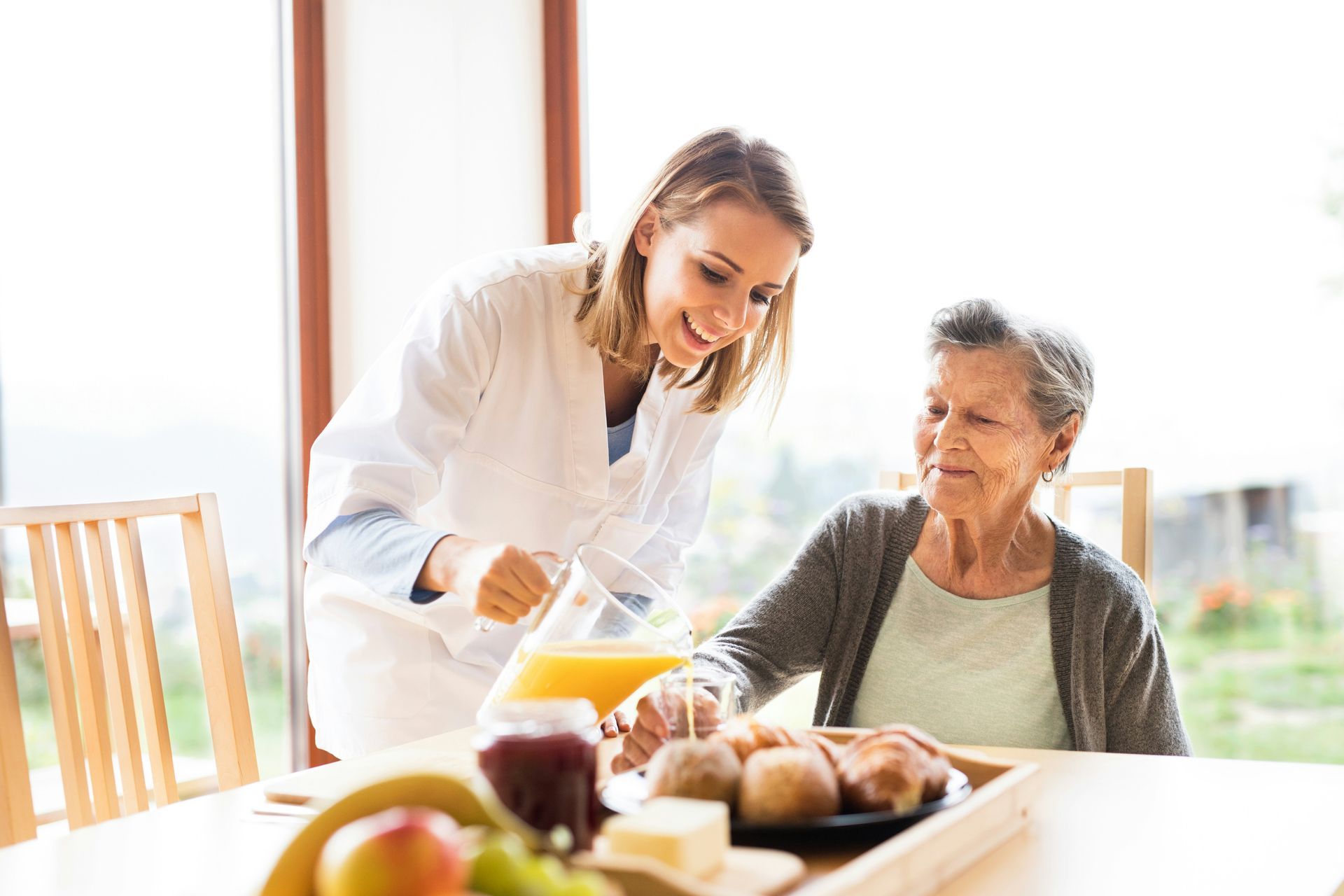 Woman pouring juice for older woman at table set for breakfast.
