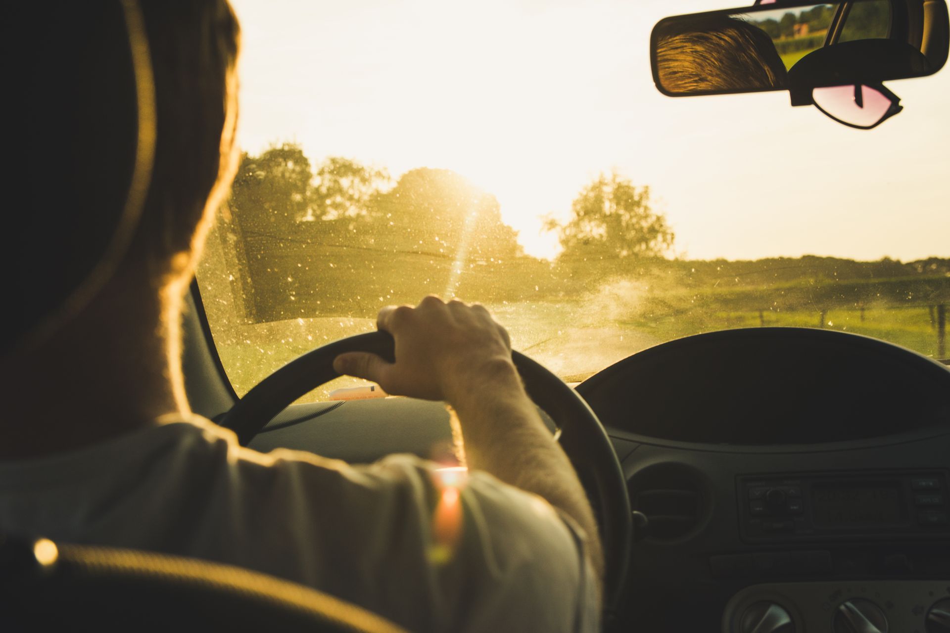 Person driving a car toward the setting sun. Golden light shines through the windshield.