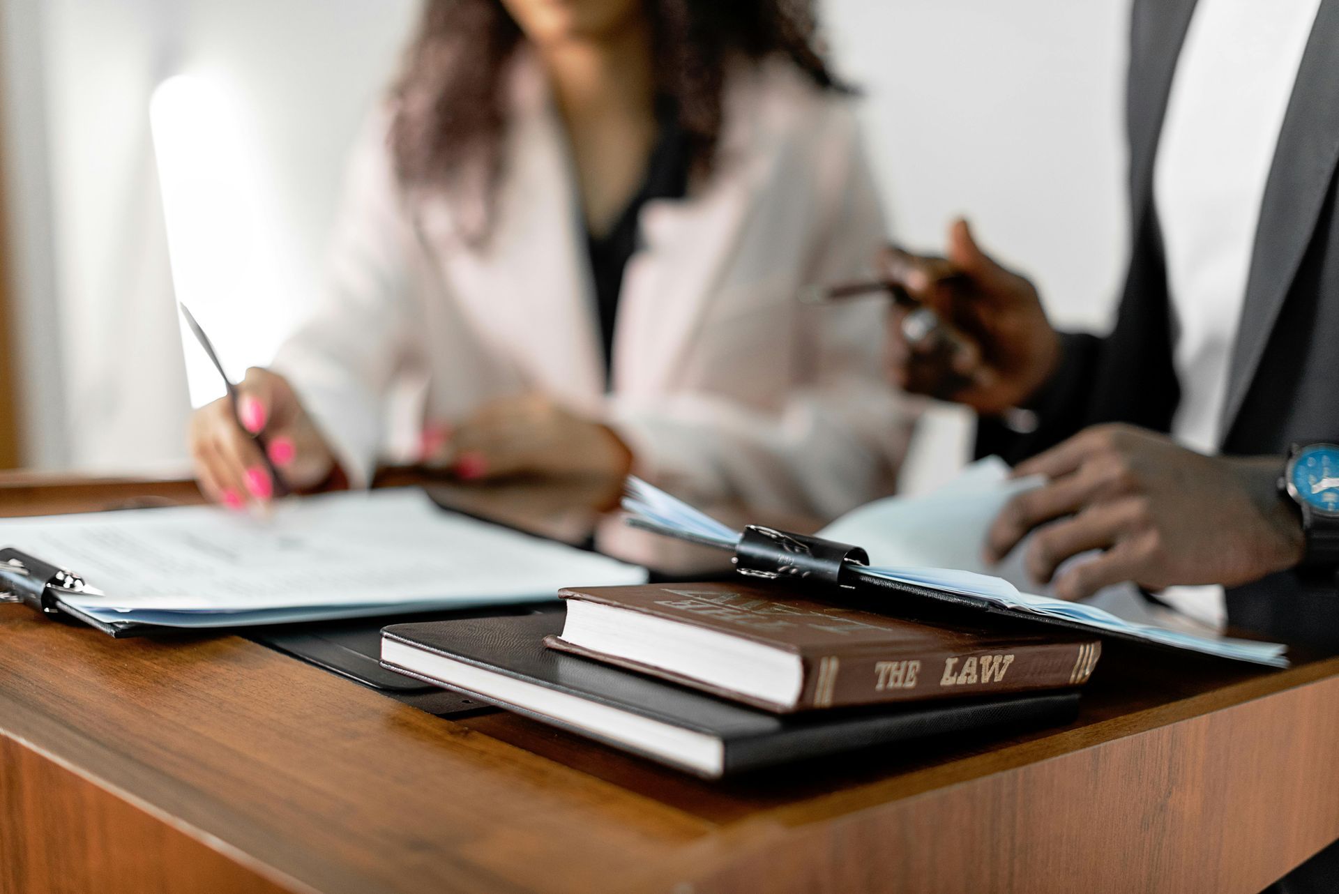 Two people review documents, with a law book on a desk.