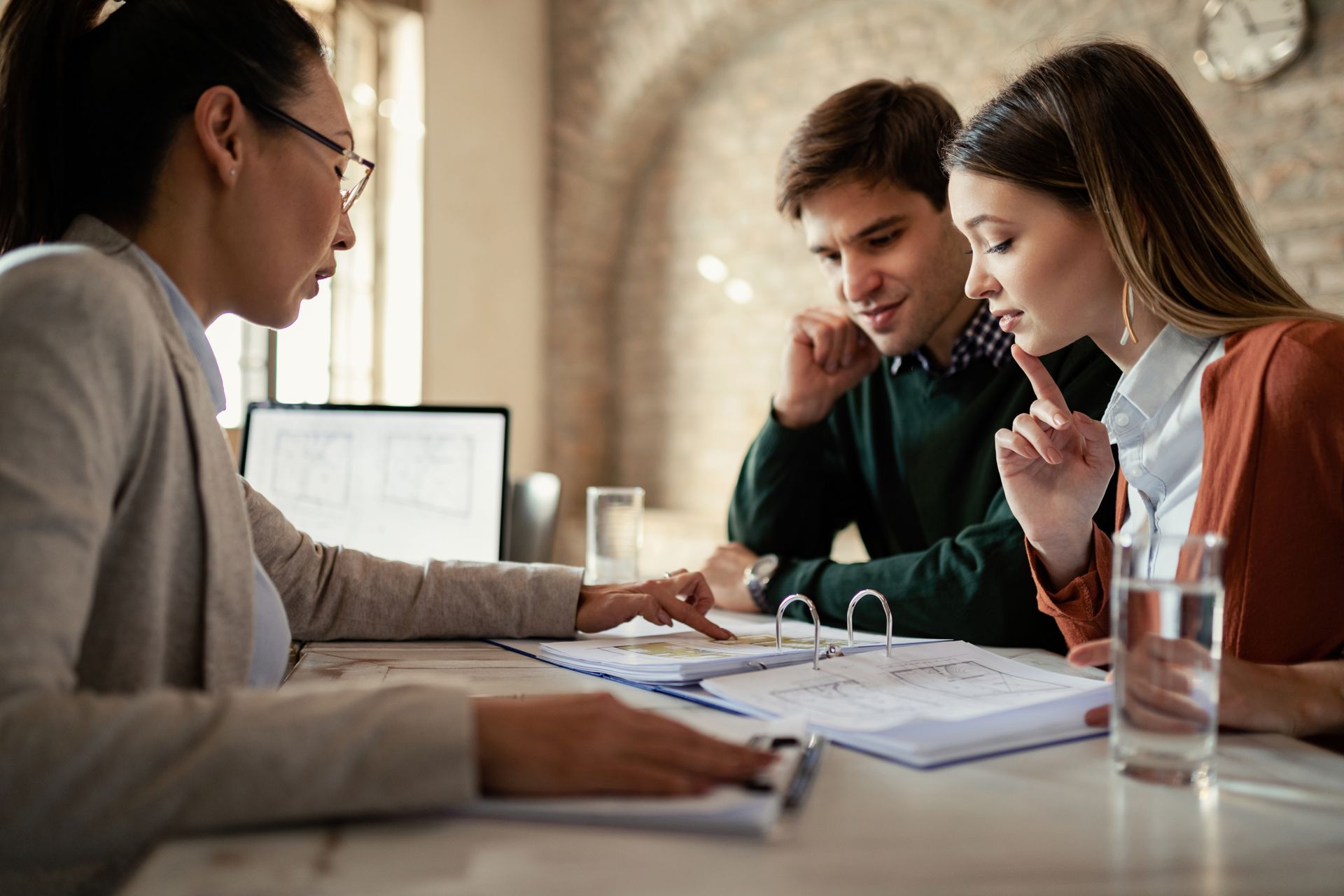 Woman in blazer pointing at documents with couple at table.