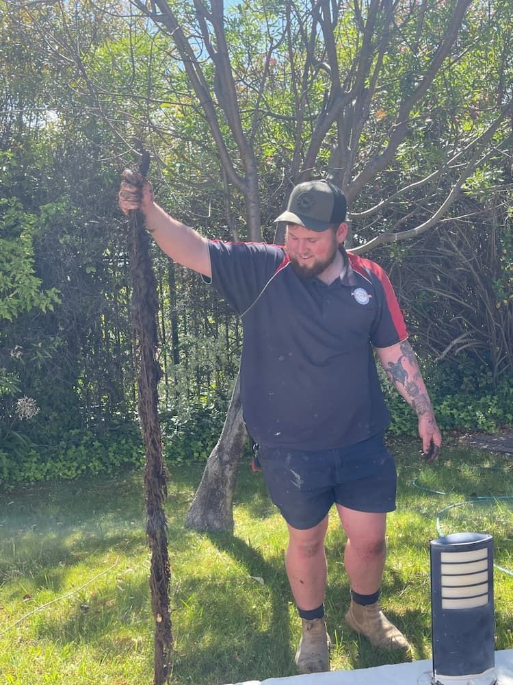 A Man is Standing in a Yard Holding a Pole — Around Town Plumbing Services in Belconnen, ACT