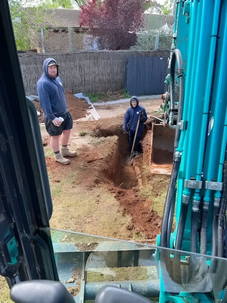 A Man is Digging a Hole in the Ground With a Shovel — Around Town Plumbing Services in Canberra, ACT