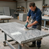 Un trabajador lija una encimera de granito sobre una mesa con ruedas en un taller.
