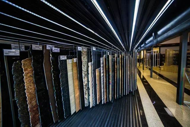 Estantes con muestras de telas colgantes en una moderna sala de exposición con luces brillantes en el techo y paredes reflectantes.