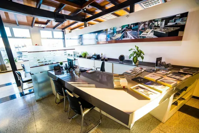 Sala de conferencias moderna con mesa grande, sillas, plantas y mucha luz natural.