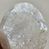 Primer plano de un cristal blanco, rugoso y translúcido, con superficies facetadas y pequeñas motas marrones.