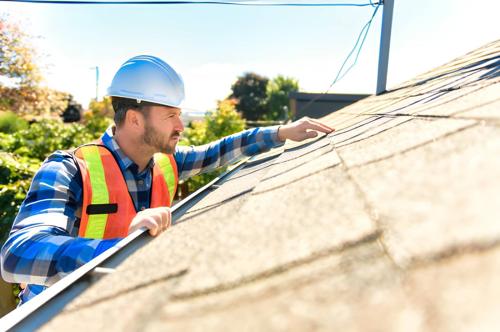 Construction worker in hard hat and safety vest inspecting a rooftop under bright sunlight