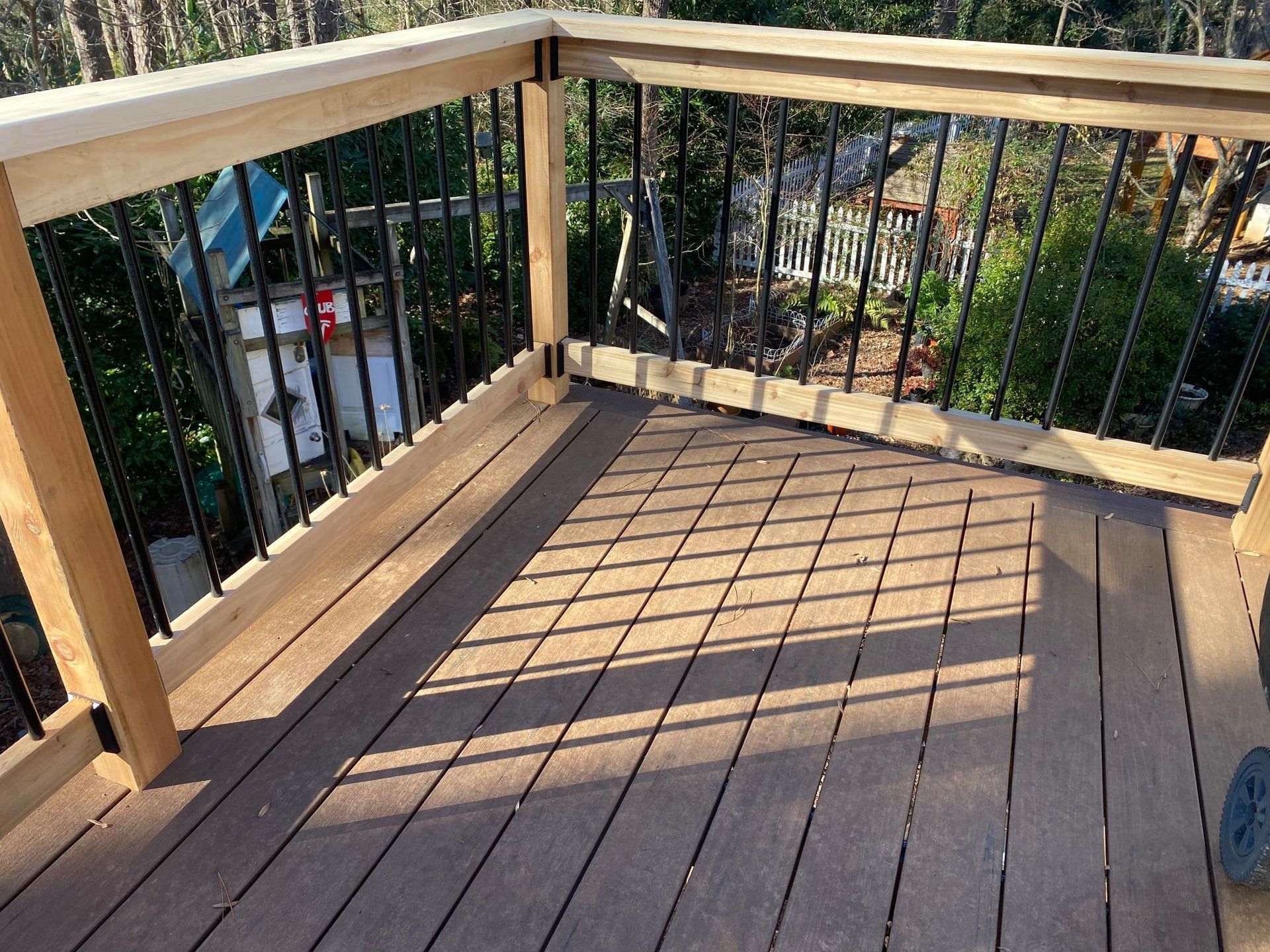 Wooden deck with black railing and light brown decking; sunny outdoor setting.